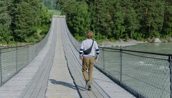Image of a student walking across a wooden bridge over a wide river