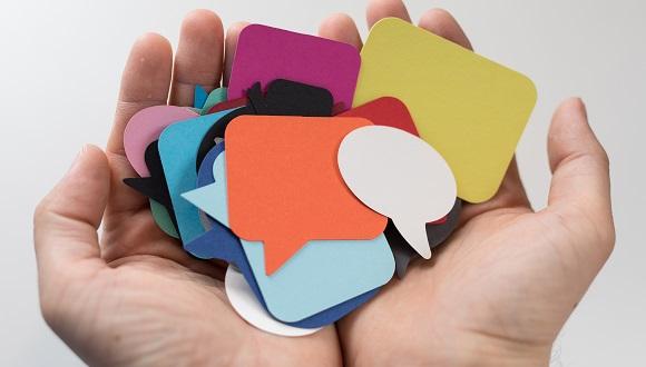 A pair of open hands holding lots of multi-coloured Post-it notes in the shape of speech bubbles