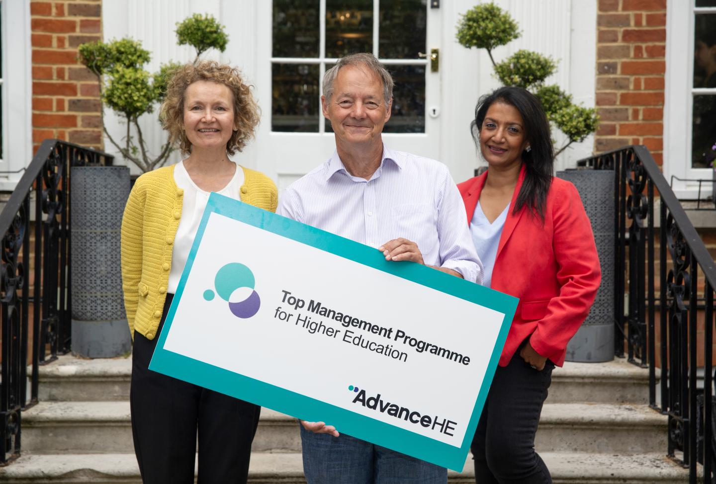 Two women and a man with a sign which says 'Top Management Programme'