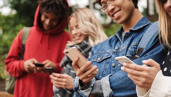 A group of diverse students looking at smartphones and smiling