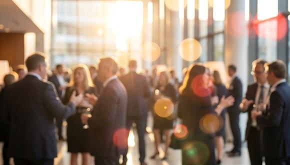 Blurred professionals are actively networking and conversing in a sun-drenched, spacious modern lobby during an event.